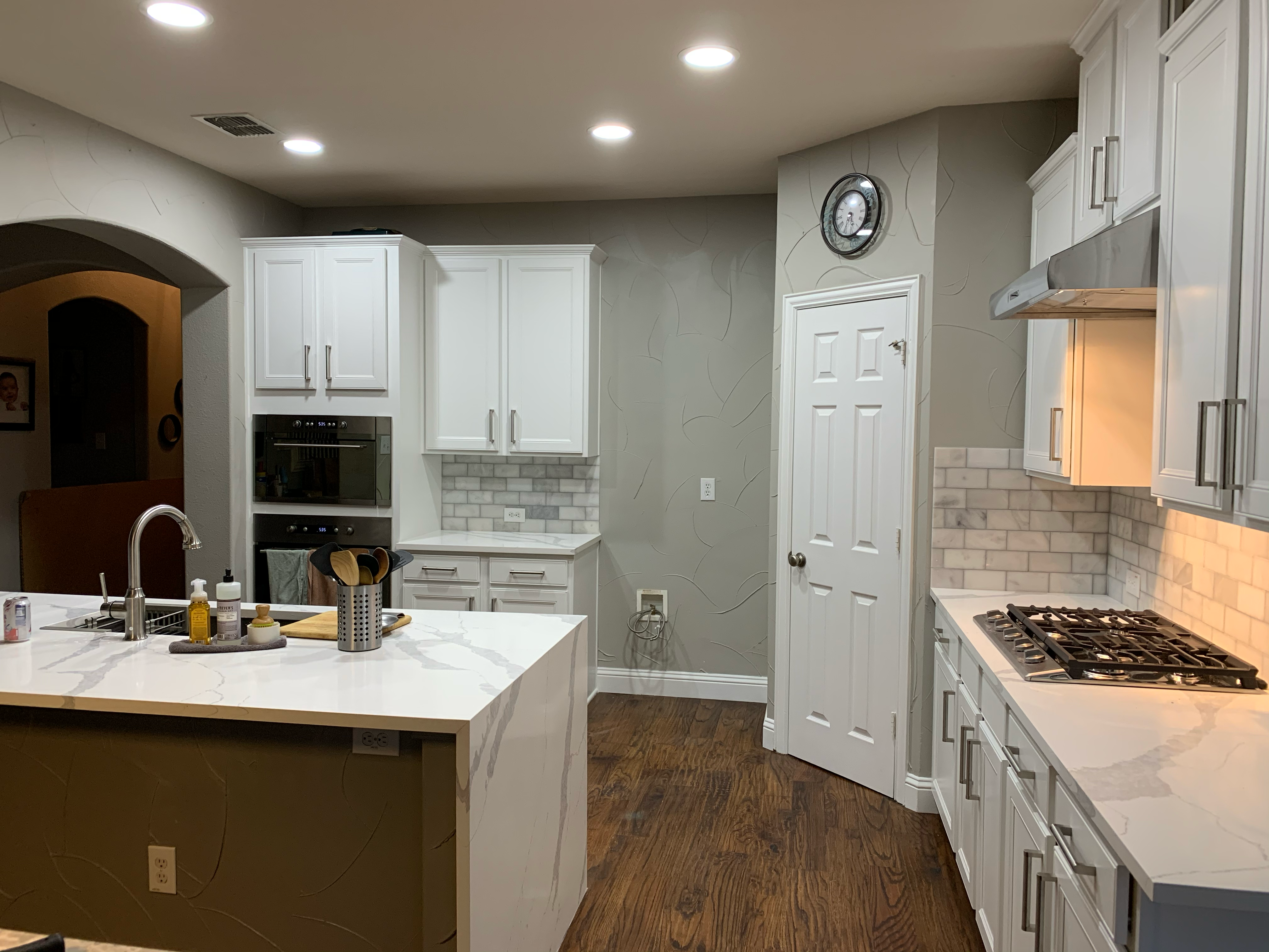 Built-in wall ovens beside a pantry door and quartz island