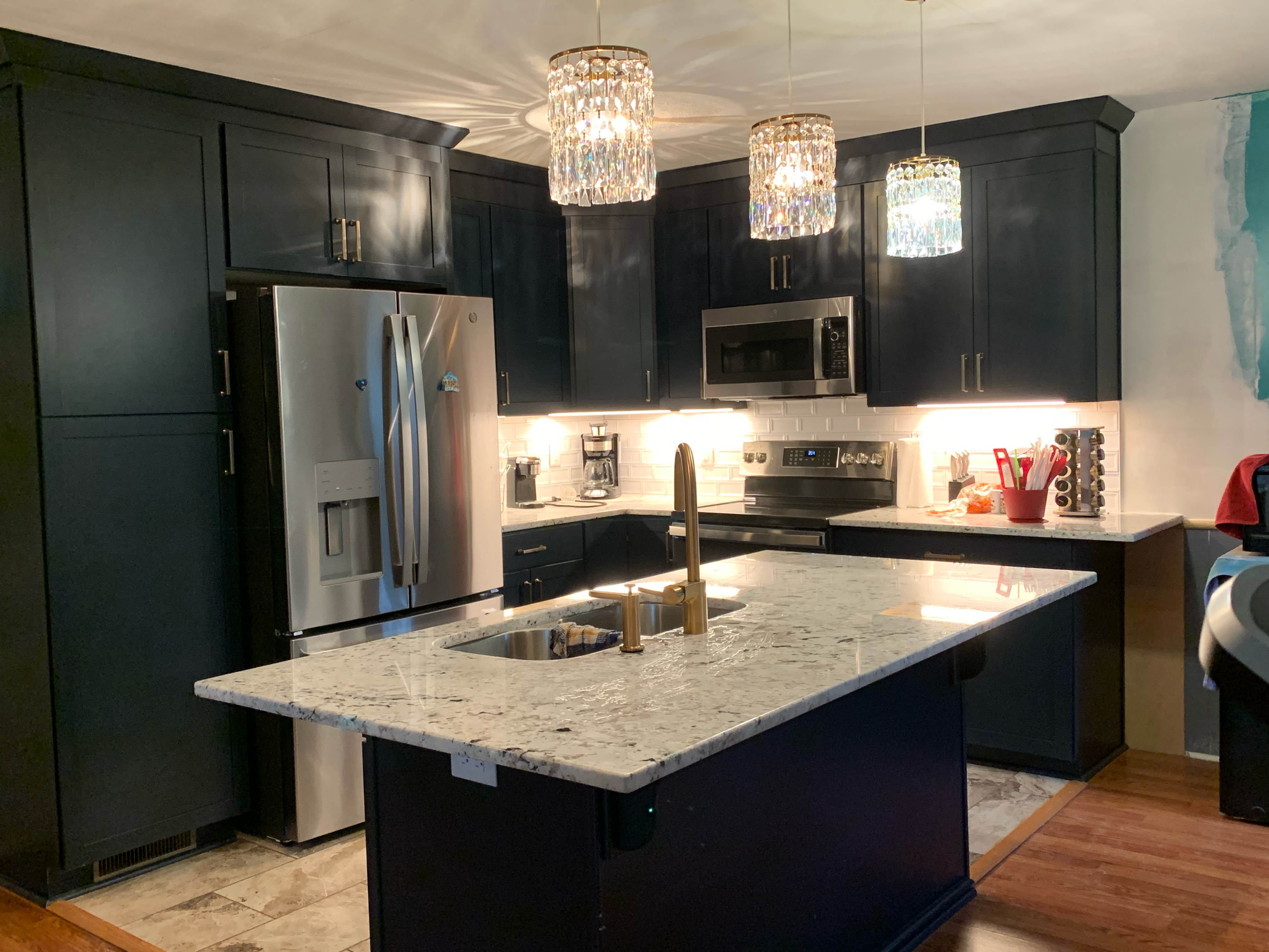 Dark navy kitchen island with granite countertop, gold faucet, and crystal pendant lights