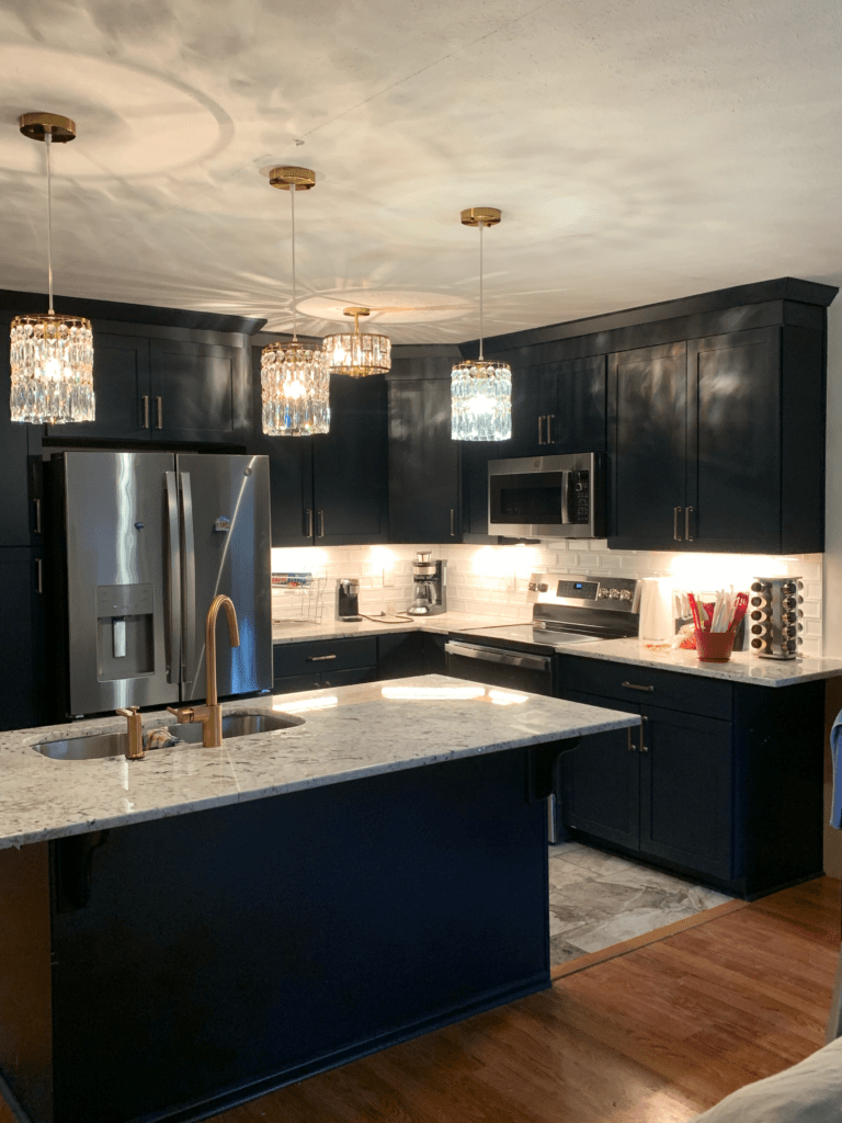 Full view of a navy cabinet kitchen with layered crystal chandelier pendants