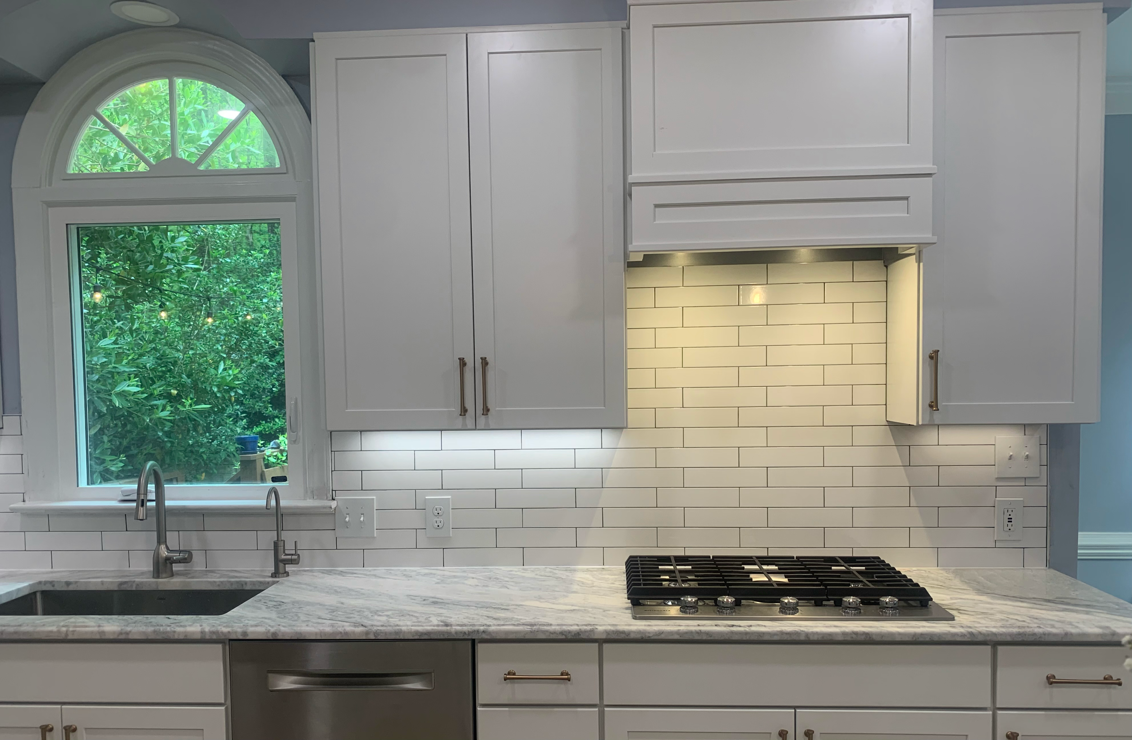 Arched transom window above a sink with dual faucets and marble-look countertop